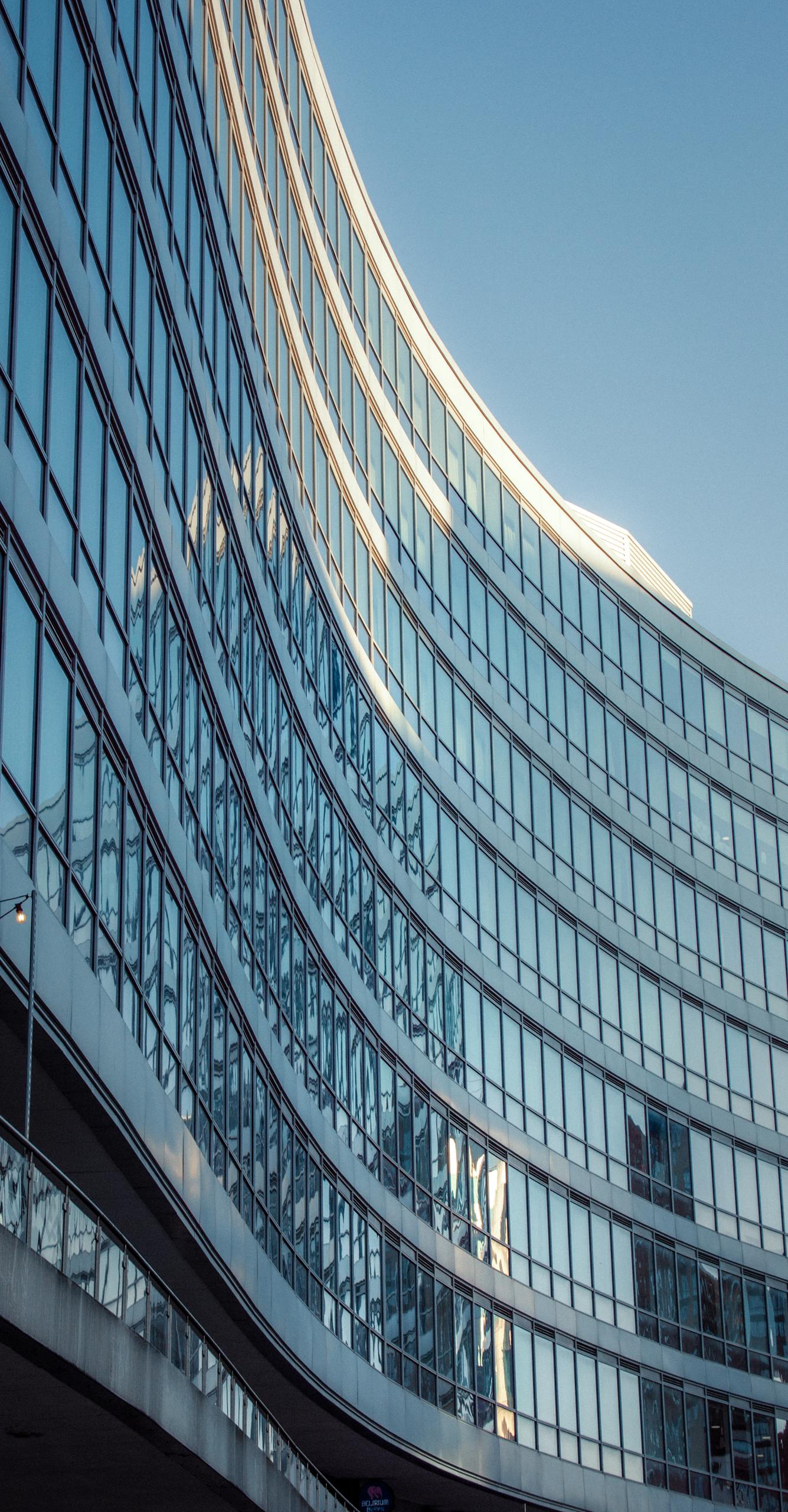 photo by daniel wells Modern curved glass building facade in Manchester, United Kingdom at sunset.